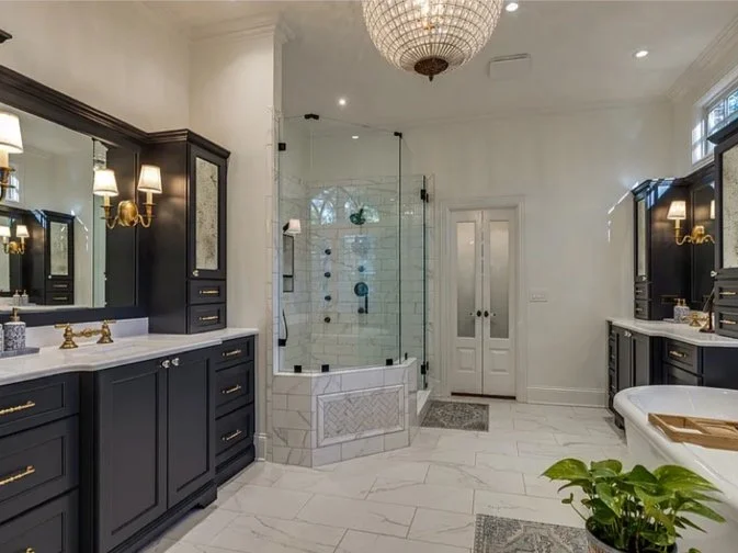 Elegant bathroom with double vanity sinks, black cabinetry, a glass shower with white subway tiles, and a freestanding bathtub.