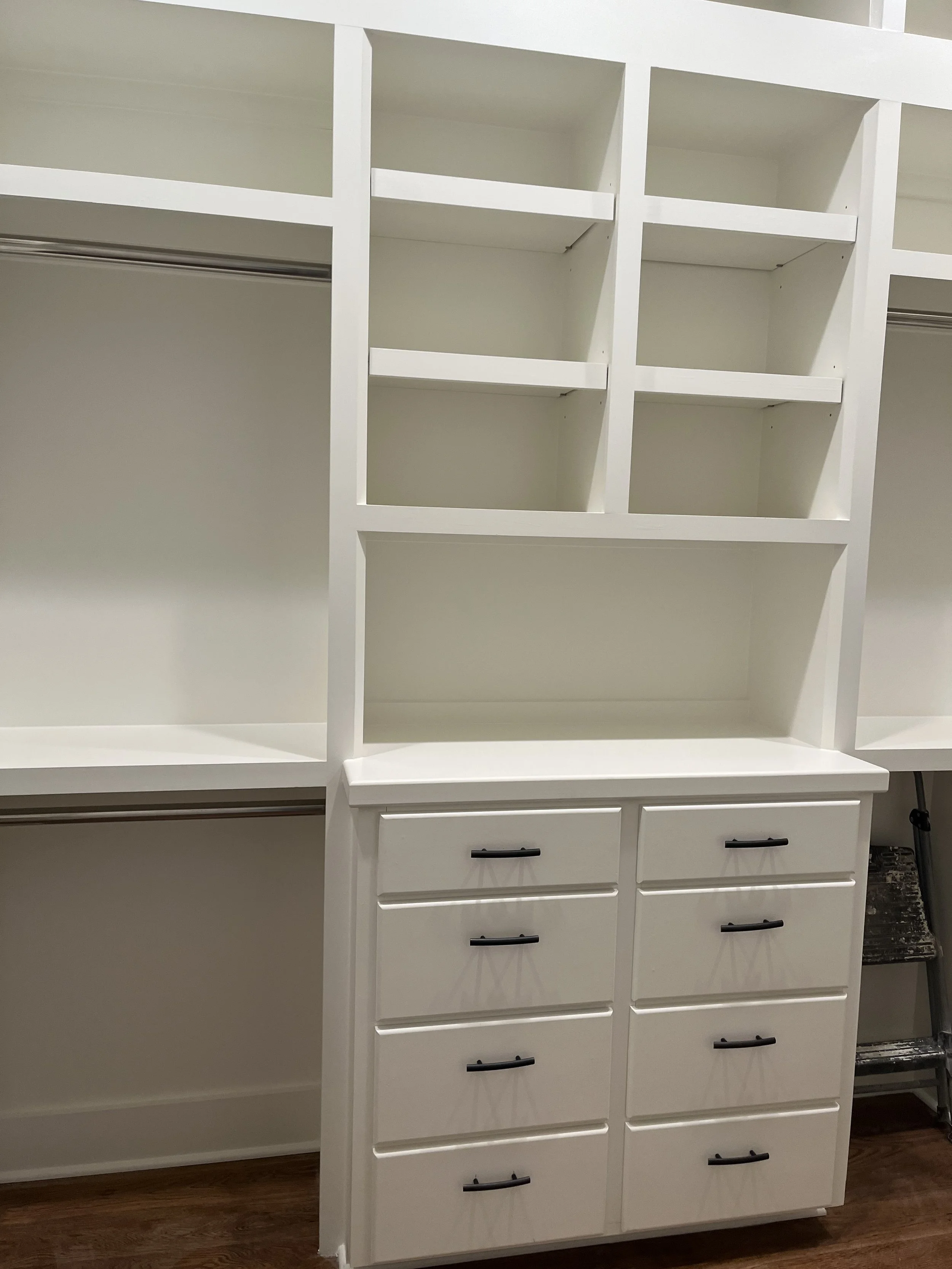 Empty white closet with open shelving and drawers, hardwood floor.