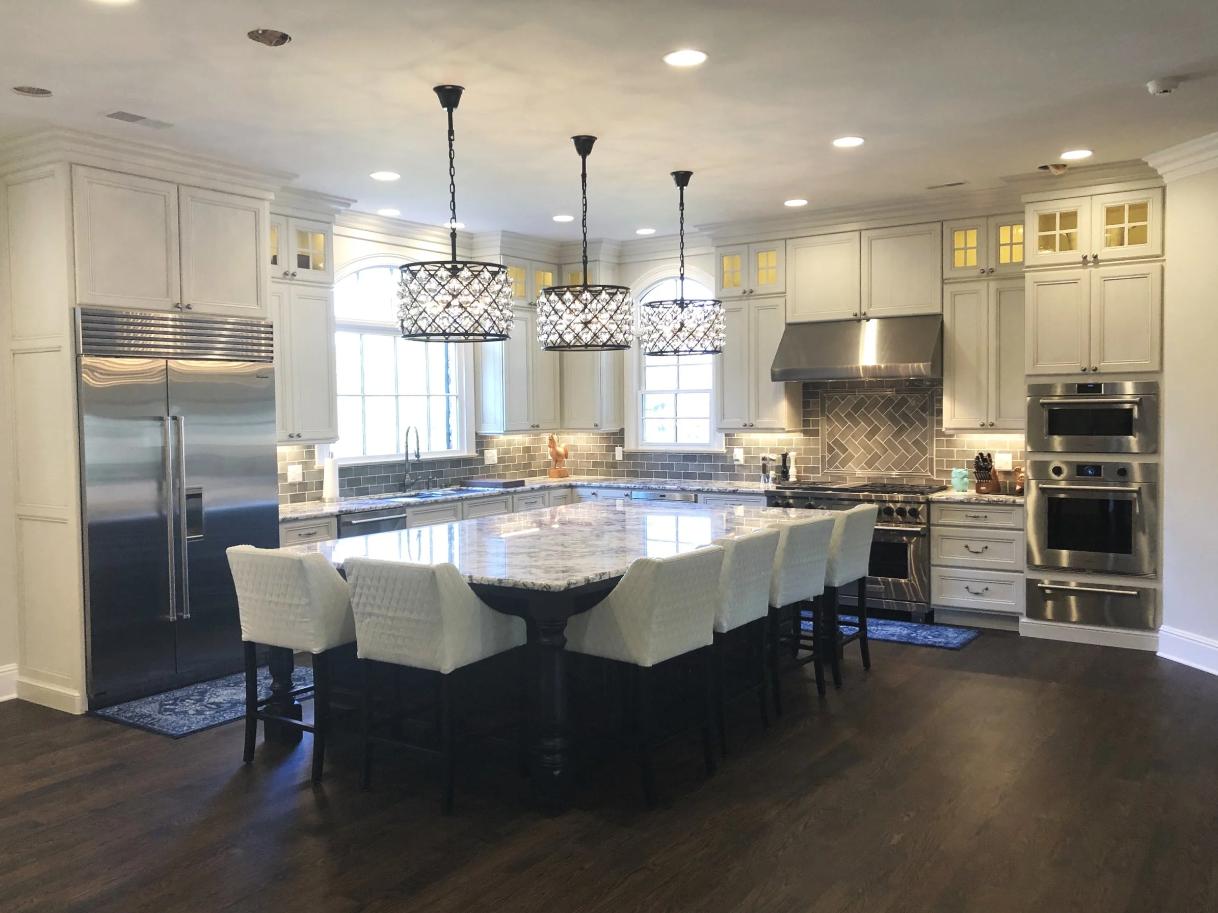 Modern kitchen with white cabinets, gray backsplash, stainless steel appliances, granite island, and three hanging pendant lights.