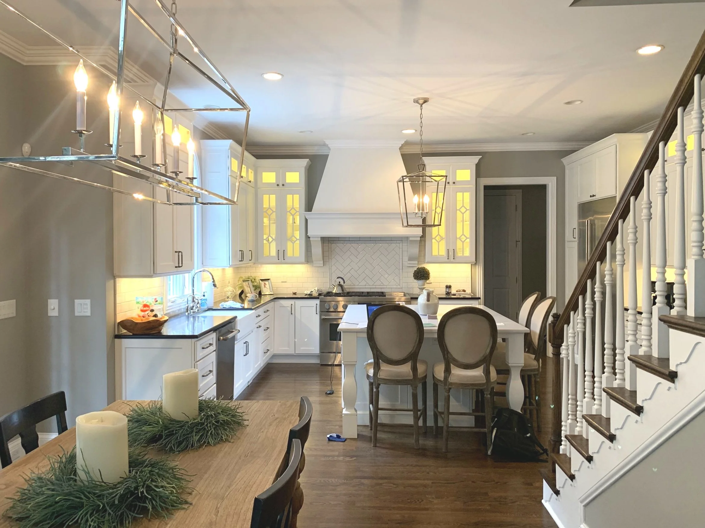 A modern kitchen with white cabinets, a central island, a dining table with candles, and a staircase to the right.