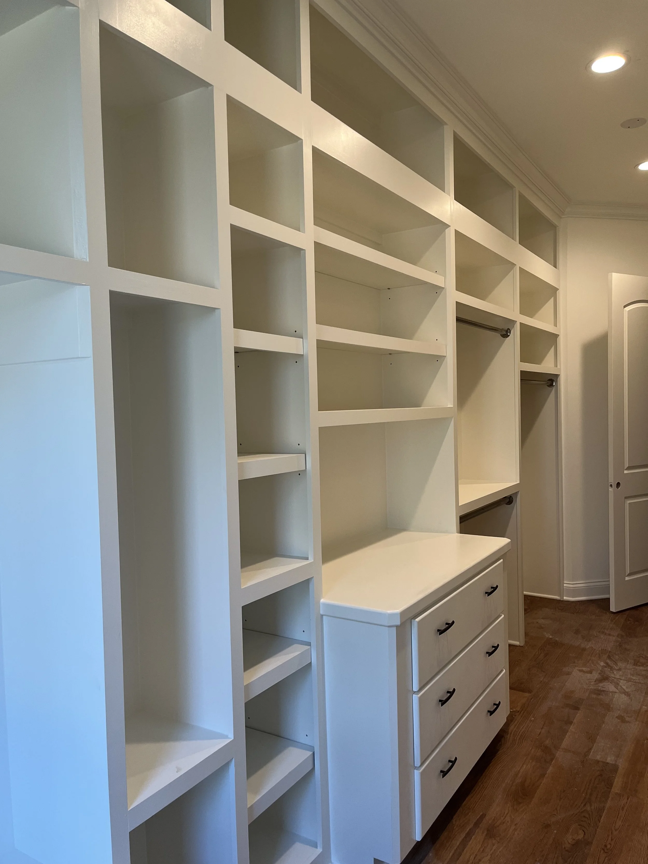 Empty white shelving unit with drawers in a room with hardwood floor.