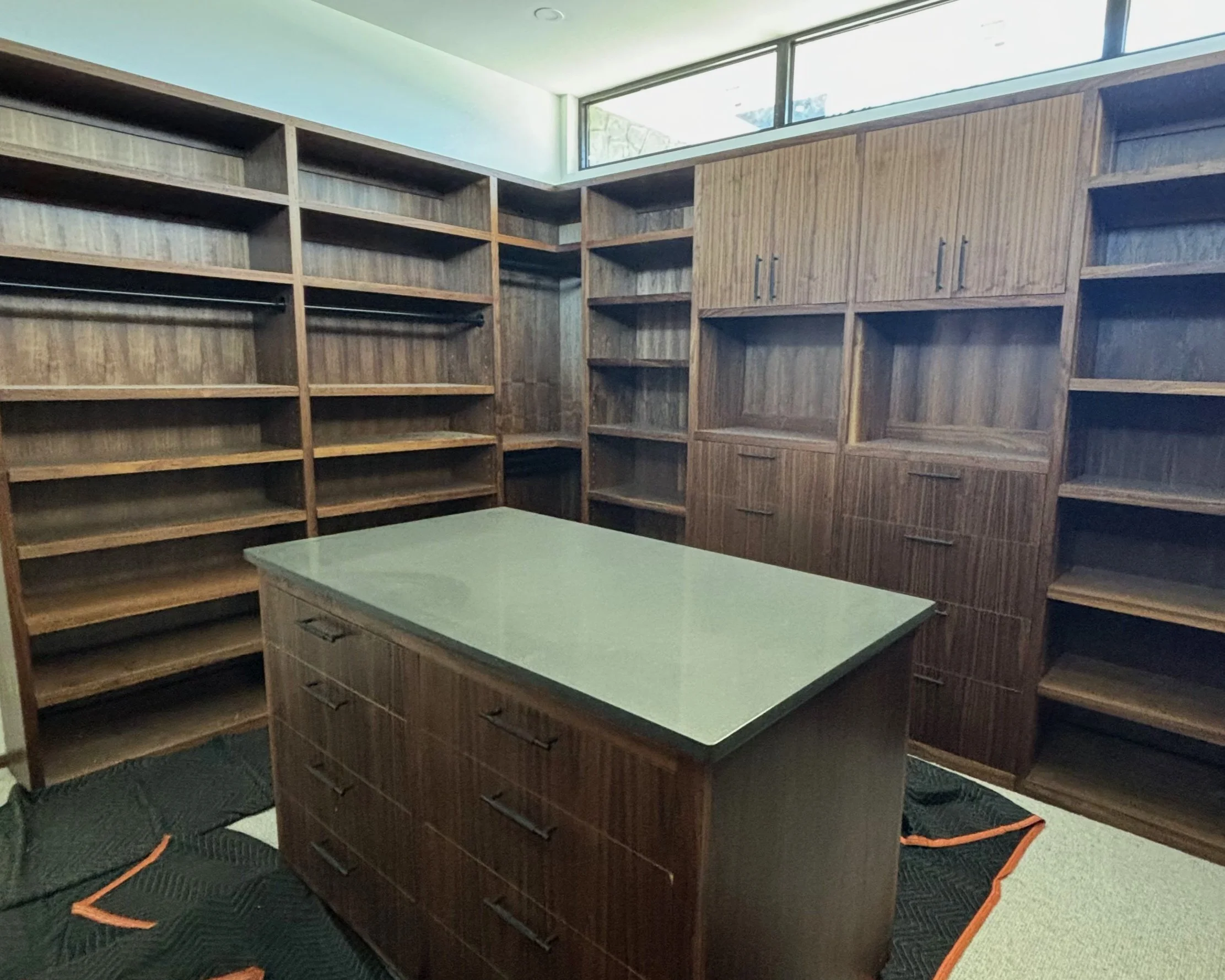 Empty walk-in closet with wooden shelves and a central dresser with a white countertop.