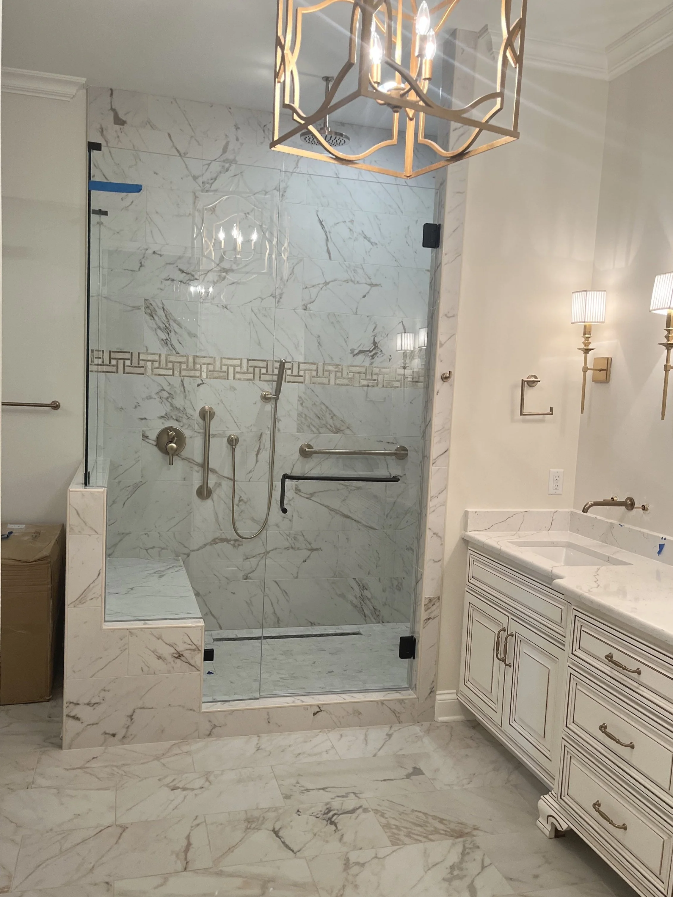 Bathroom with marble tiles, a glass shower with metal fixtures, a white vanity with a marble countertop, and wall-mounted lights.