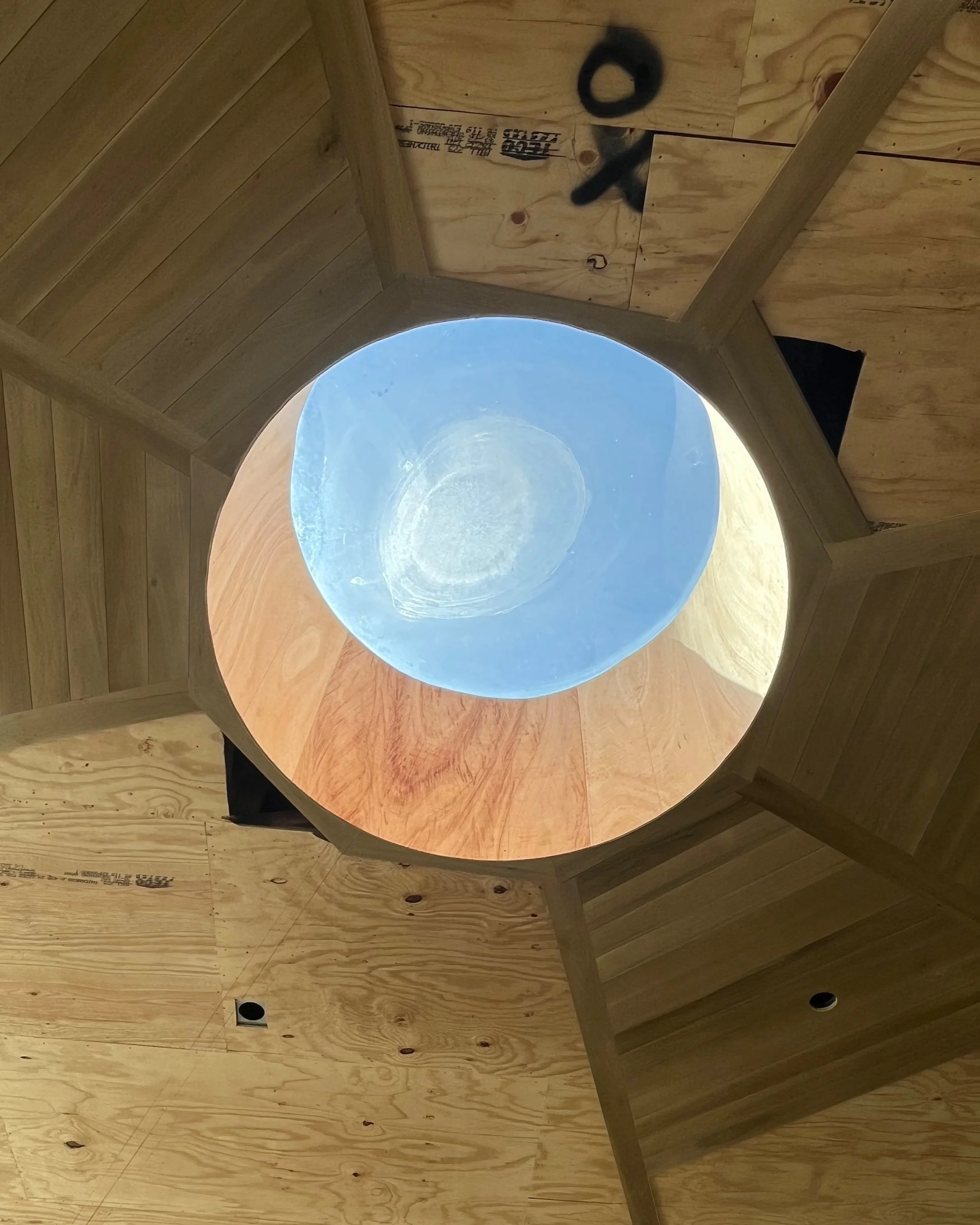 A circular hole in a wooden ceiling or floor, looking up through it at the sky