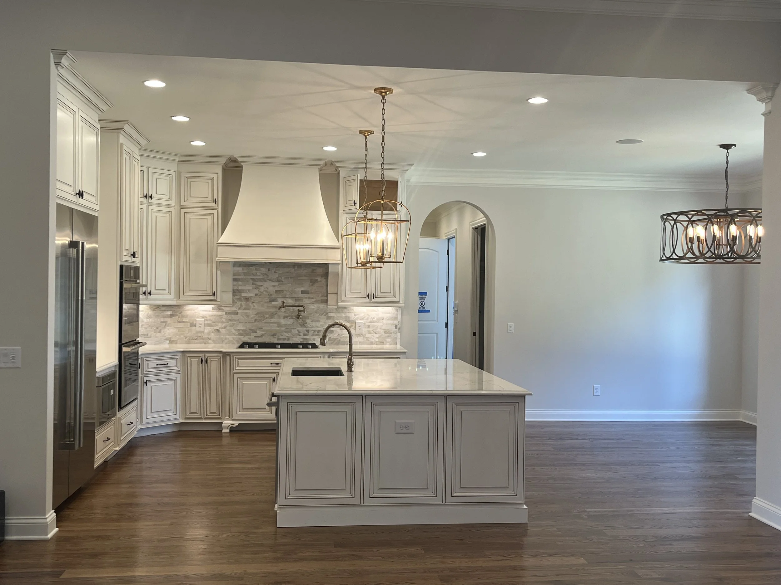 Modern kitchen with white cabinetry, marble countertops, wooden flooring, and two chandeliers.