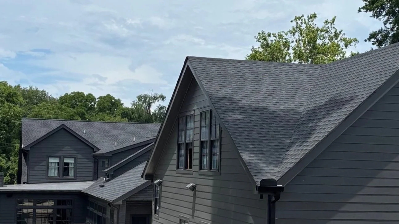 Backyard of a modern house with a swimming pool, children's play area, and dark gray siding, set in a green backyard under a partly cloudy sky.