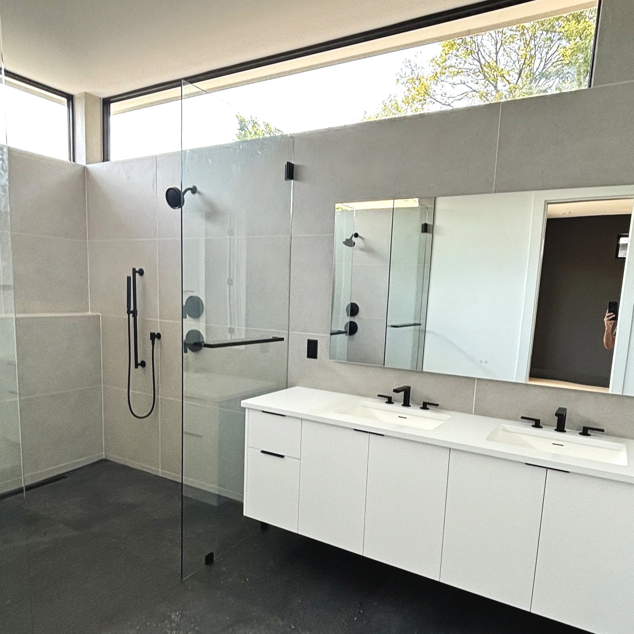 Modern bathroom with a double sink vanity, large mirror, and walk-in shower with glass partition and black fixtures.